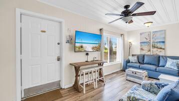 A living room with a television, a ceiling fan, a sofa, a coffee table, and a wooden bench.