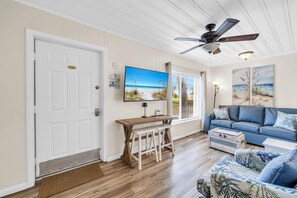 A living room with a television, a ceiling fan, a sofa, a coffee table, and a wooden bench. - Linda's Cozy Cottage A (Panama City Beach)