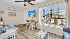 A room with a ceiling fan, a TV, a wooden table with chairs, a sofa, and a large window with blinds. - Linda's Cozy Cottage A (Panama City Beach)