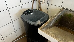 Een zwarte prullenbak met een digitale weegschaal, een betegelde muur en een houten vloer.