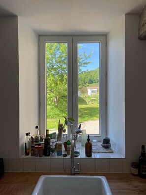 Eine Küche mit einem großen Fenster, einer Spüle und verschiedenen Küchenutensilien auf der Fensterbank.