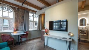 A modern interior with exposed brick walls, a herringbone wood floor, a dining area with red chairs, a white table, and a large TV mounted on the wall. - Studio Urbain (Alkmaar)