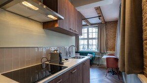 A modern kitchen with a built-in stove, a window with curtains, and a dining area with a table and chairs. - Studio Urbain (Alkmaar)