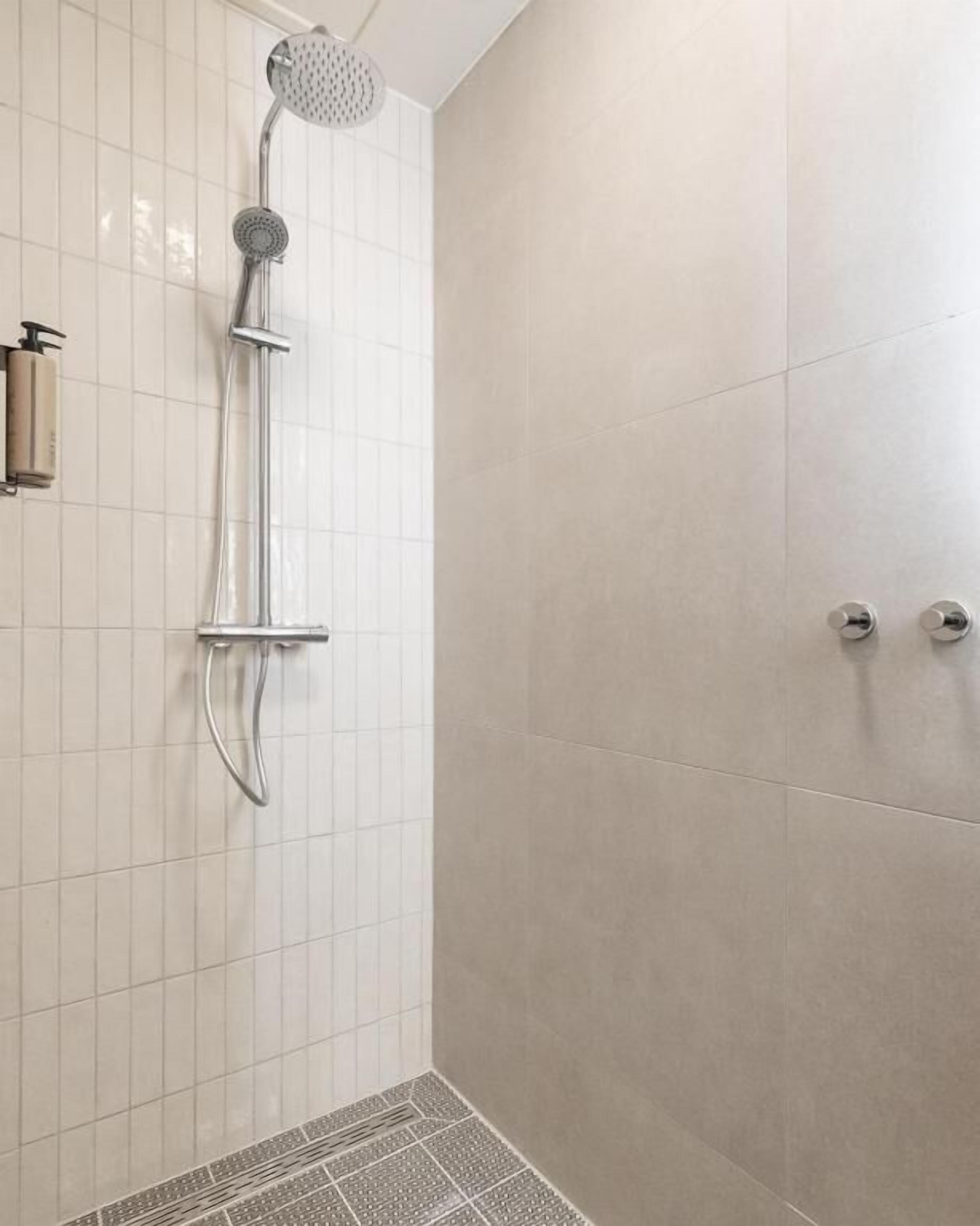 A shower with a handheld showerhead and a wall-mounted control panel.
