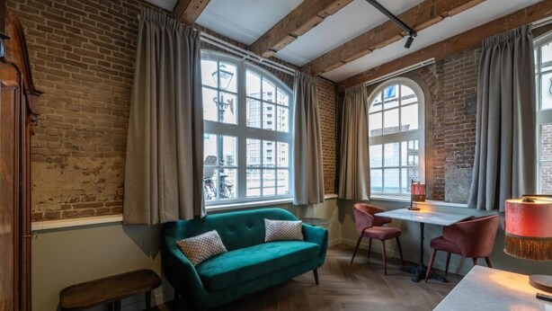 A room with a green sofa, a small table, chairs, and a lamp. - Studio Urbain (Alkmaar)