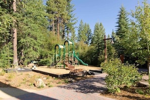 Ein Spielplatz mit Rutsche und Klettergerüsten, umgeben von Bäumen.