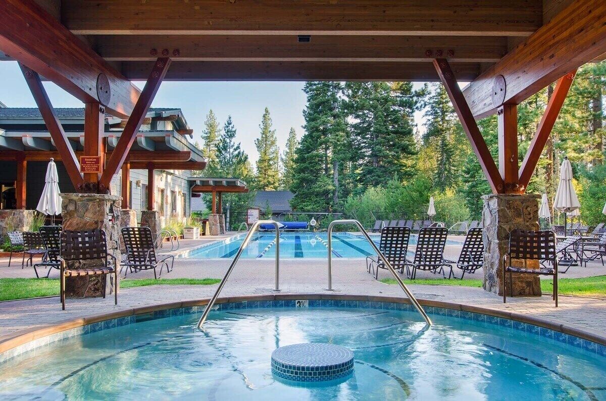 A pool area with a view of a building, surrounded by chairs and trees.