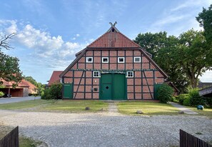 En traditionel bindingsværksbygning med en grøn dør og vinduer, omgivet af en brostensbelagt indkørsel og grøn bevoksning.
