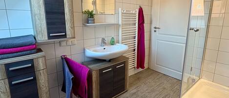 A modern bathroom with a sink, mirror, towel rack, and shower.