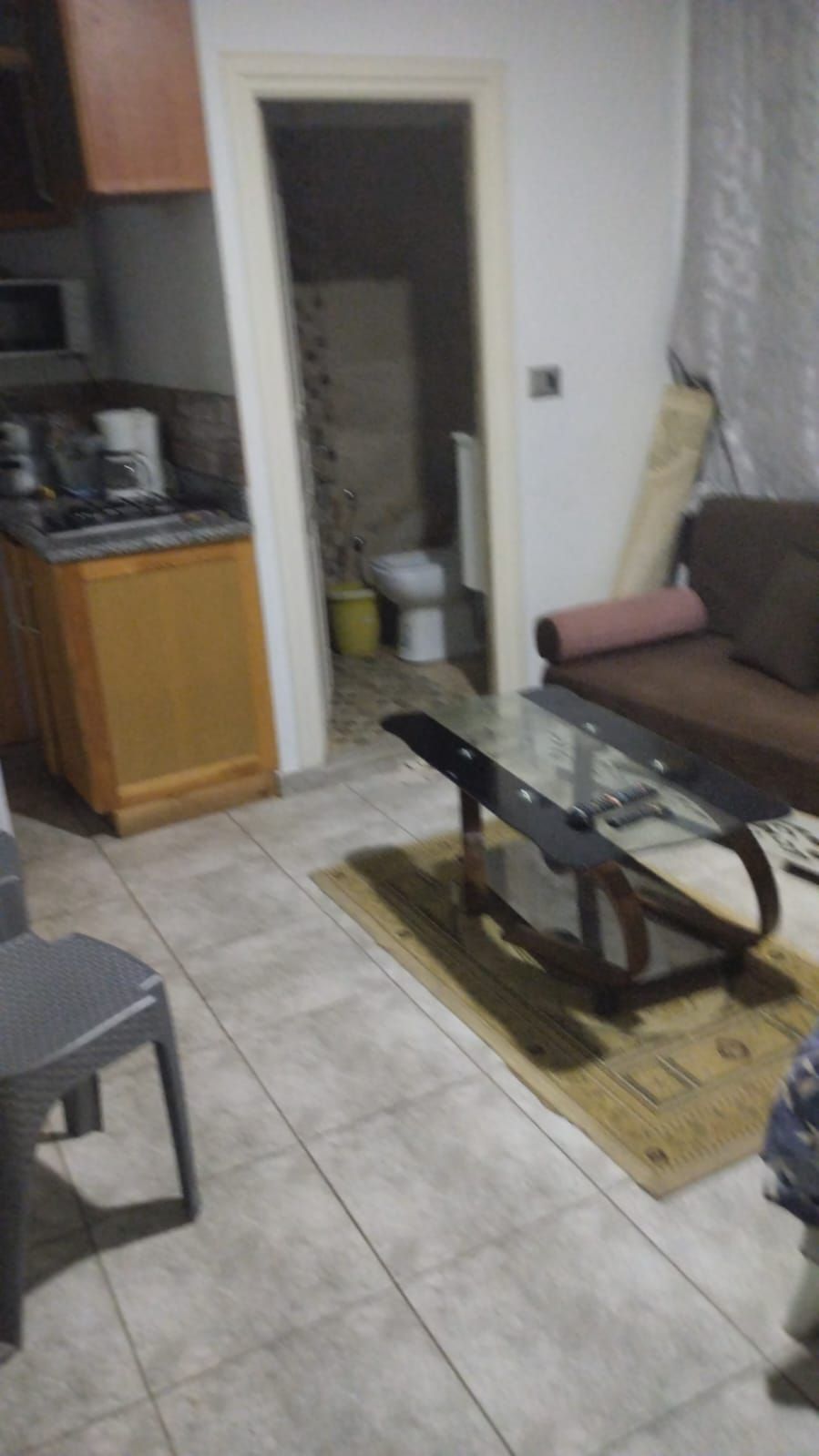 A living room with a glass-top coffee table, a sofa, and a dining area with a kitchen counter.