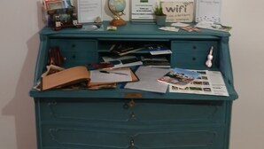 Un bureau de couleur turquoise, avec des papiers, un globe terrestre et des photos encadrées accrochées au mur derrière.