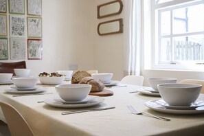 A dining table set with white bowls, plates, and cutlery, with a loaf of bread and a bowl of salad on the table. - Abbey Cottages Heron House (Talley)