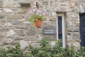 Ein Steinhaus mit einem Schild, auf dem 'TYR CRYCHYDD HERON HOUSE' steht, und einem hängenden Blumentopf.