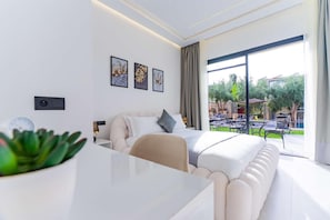 A modern hotel room with a large bed, a dining table, and a view of the outdoor patio. - Villa Zahi (Tameslouht)