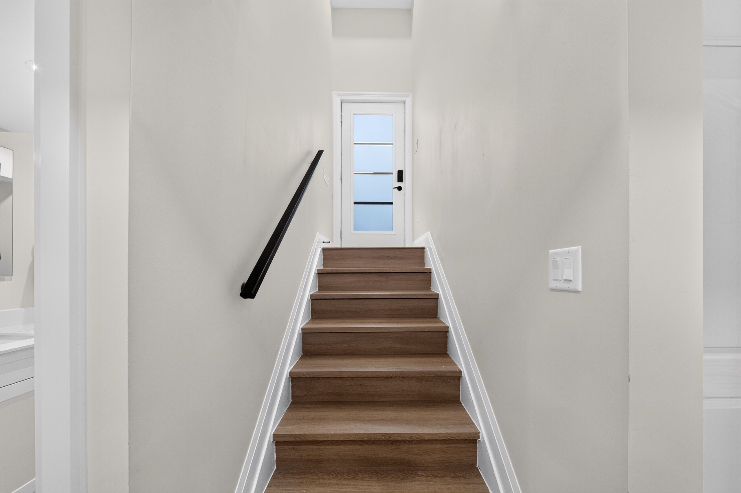 Una escalera de madera con paredes blancas que conduce a una puerta con un panel de vidrio esmerilado.