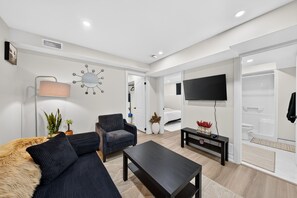 Un salon moderne comprenant un canapé, un fauteuil, une table basse et un téléviseur à écran plat.