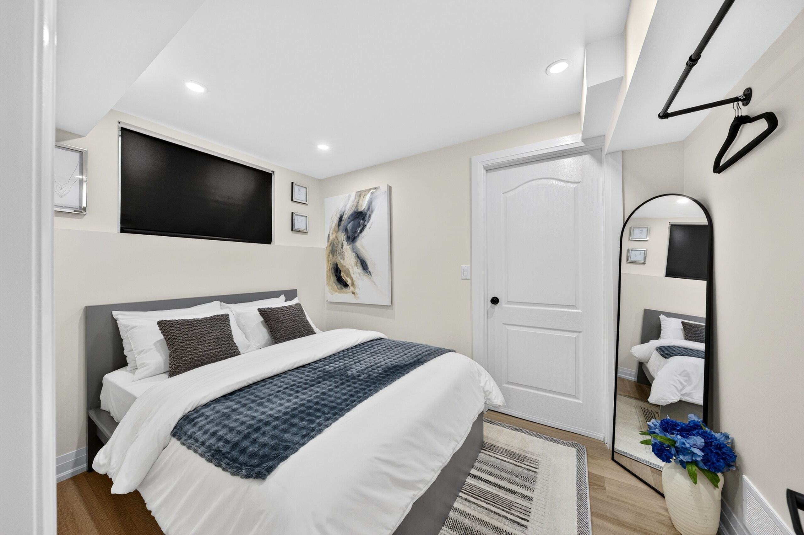 A modern bedroom with a bed, a large mirror, a door, and a wall-mounted TV.