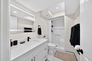 Une salle de bain moderne avec un meuble-lavabo blanc, un grand miroir, des toilettes et un espace douche.