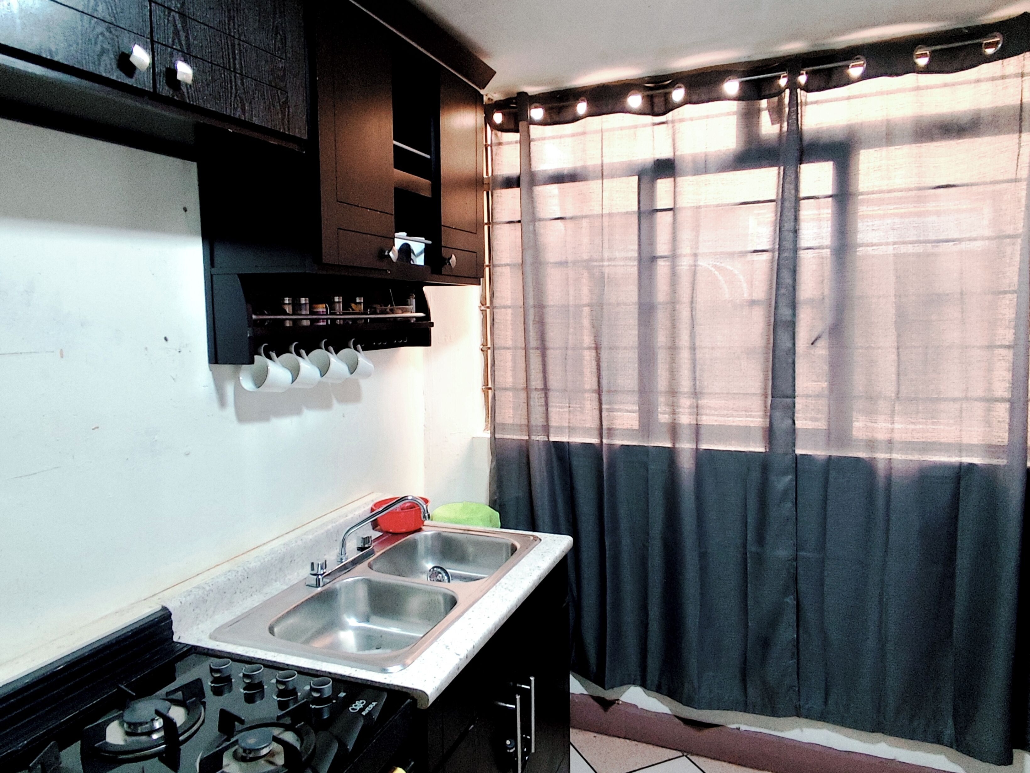 A kitchen with a gas stove, double sink, and a window with curtains.