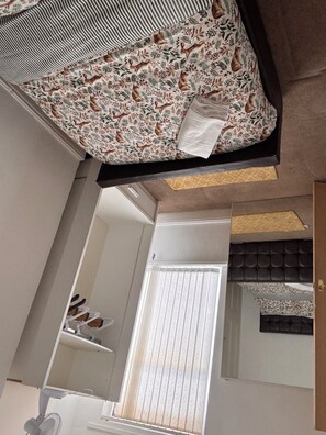 A room with a bed, a window with blinds, a ceiling fan, and a mirror.