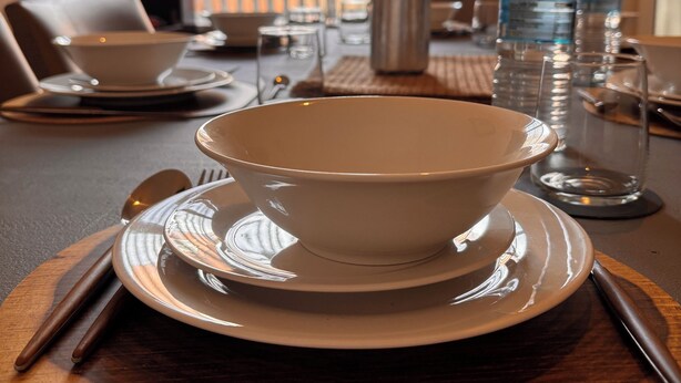 Una mesa de comedor preparada con un bol, platos, cubiertos y botellas de agua.