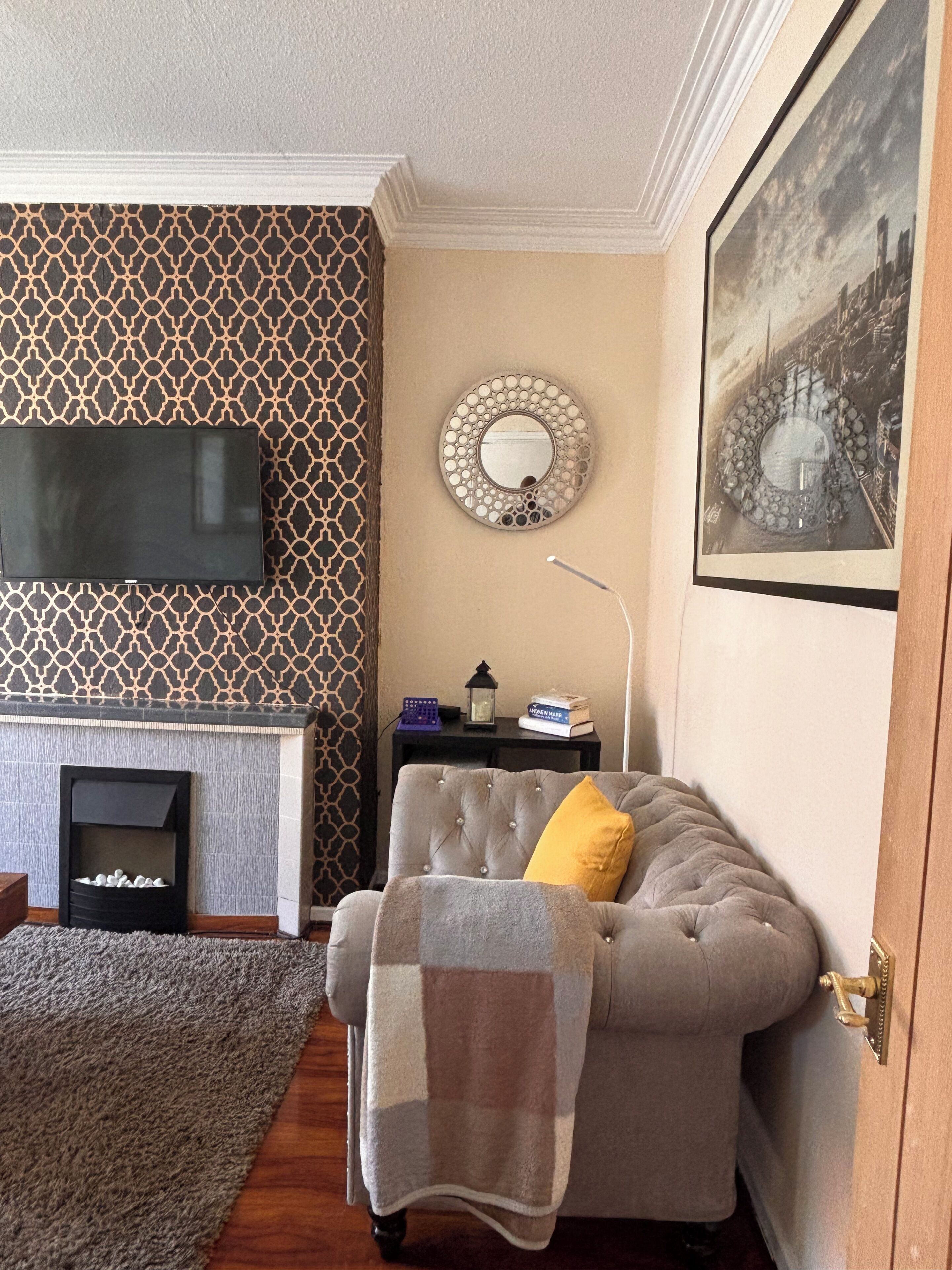 Ein Wohnzimmer mit Kamin, einer Couch, einem Fernseher, einer Wand mit Muster und einem gerahmten Bild.