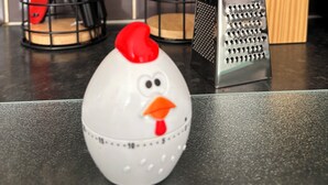 Una encimera de cocina con distintos utensilios, un rallador y un salero decorativo con forma de gallina.