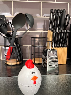 A kitchen counter with various utensils, a grater, and a decorative chicken-shaped salt shaker.