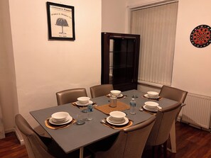 A dining room with a table set for four, a framed picture on the wall, and a dartboard. - Spacious 4BR Home | Sleeps 7 | 2 Baths | Long Stays (Manchester)