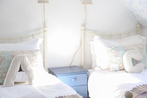Uma cama com roupa de cama branca, uma mesa de cabeceira azul e um travesseiro com um mapa-múndi.