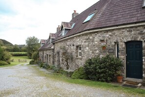 Ein Steinhaus mit einer dunklen Tür, einem Kiesweg und einer grünen Landschaft.