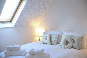 Ein Schlafzimmer mit Dachfenster, einem Bett mit weißen Leinen und dekorativen Kissen mit Weltkartenmuster.