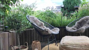 Eine Terrassenfläche mit zwei Korbstühlen, einem Gewebepuff und einem Weidenkorb.