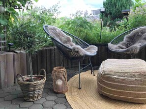 Un patio con dos sillones de mimbre, un otoman tejido y una cesta de mimbre.