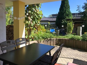 Eine Terrasse mit Tisch und Stühlen, umgeben von einem Garten mit Pflanzen und einem Zaun.