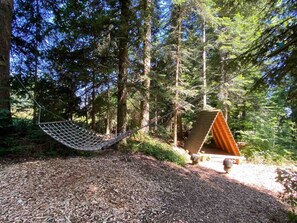 A hammock in a forested area with a wooden structure nearby.