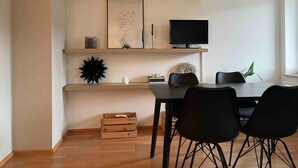 Ein moderner Essbereich mit einem Holztisch, schwarzen Stühlen, einer hängenden Leuchte und einem an der Wand befestigten Flachbildfernseher.