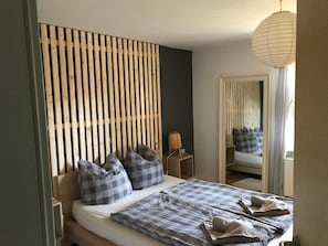 Ein Schlafzimmer mit Bett, Kissen, einem Nachttisch, einer Lampe und einem Spiegel.