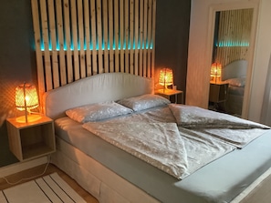 A bed with a headboard, two bedside lamps, and a bedside table.