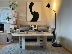 A living room with a sofa, a coffee table, a floor lamp, and a wall with a large abstract painting. - Modern Oasis of Calm in Allgäu with Private Terrace and Wi-Fi (Oberreute)