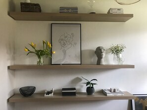 A shelf with a framed artwork, a vase with yellow flowers, a bust sculpture, and a small potted plant.