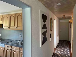 Una cocina moderna con armarios de madera, un lavamanos integrado y un pasillo con arte mural geométrico y piso estampado.