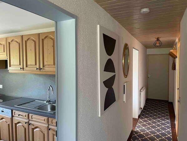 Une cuisine moderne avec des meubles en bois, un évier encastré et un couloir agrémenté d’œuvres d’art murales aux motifs géométriques et d’un sol à motifs.
