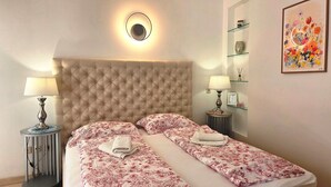 Ein Hotelzimmer mit einem gesteppten Kopfteil, zwei Nachttischen mit Lampen, einer blumigen Tagesdecke und einem gerahmten Blumenbild an der Wand.