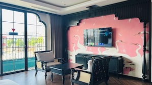 Ein Zimmer mit großem Fenster, einem flachbildfernseher an der Wand, einer Couch, einem Couchtisch und einem Schrank.