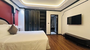 Ein Hotelzimmer mit Bett, Fernseher, einer Sitzbank, einem Schrank und einem durch eine offene Tür einsehbaren Badezimmer.