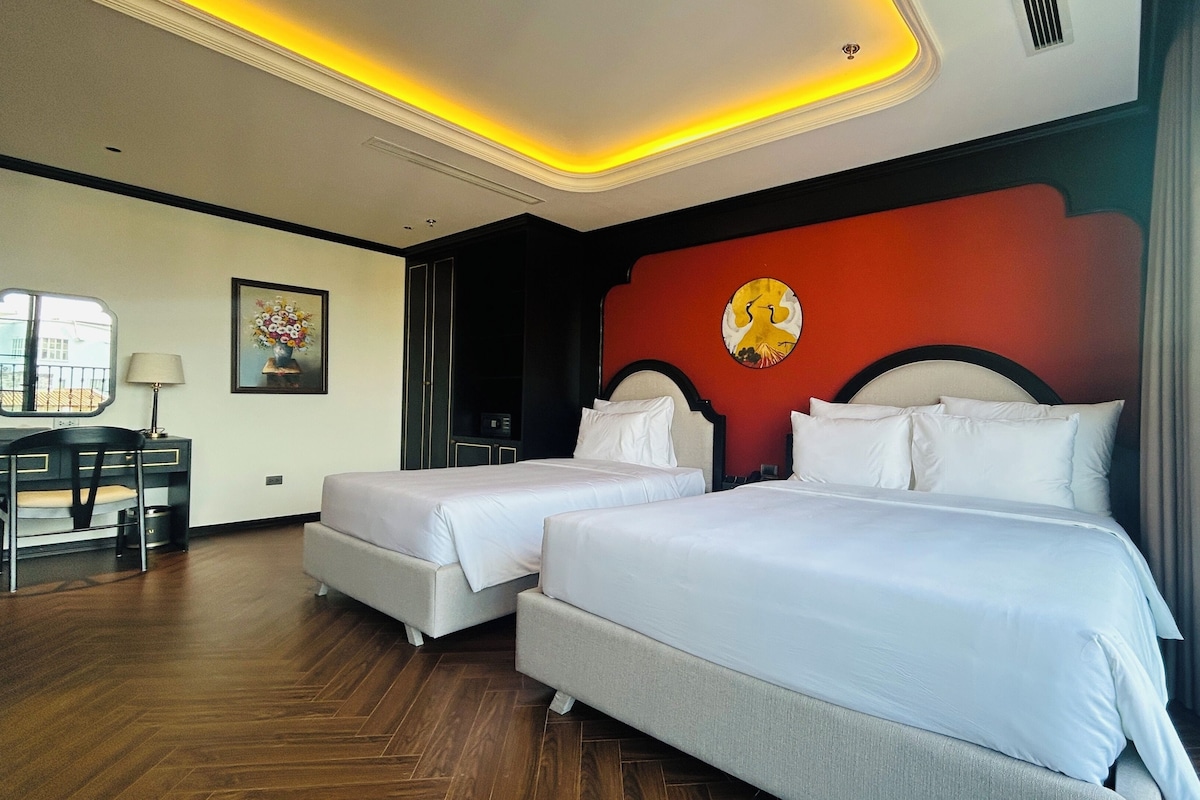 A hotel room with two beds, a desk, a chair, a mirror, and a painting on the wall.