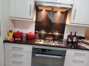 A kitchen with a gas stove, pots, a red pot, cheese sauce, and wine bottles.