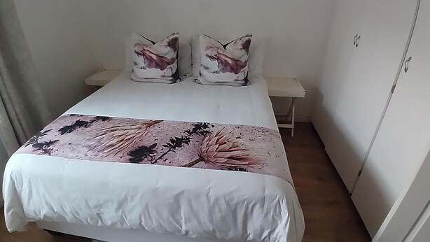 Un letto rifatto con cura, con una coperta a fiori, due cuscini coordinati e un comodino con una lampada.