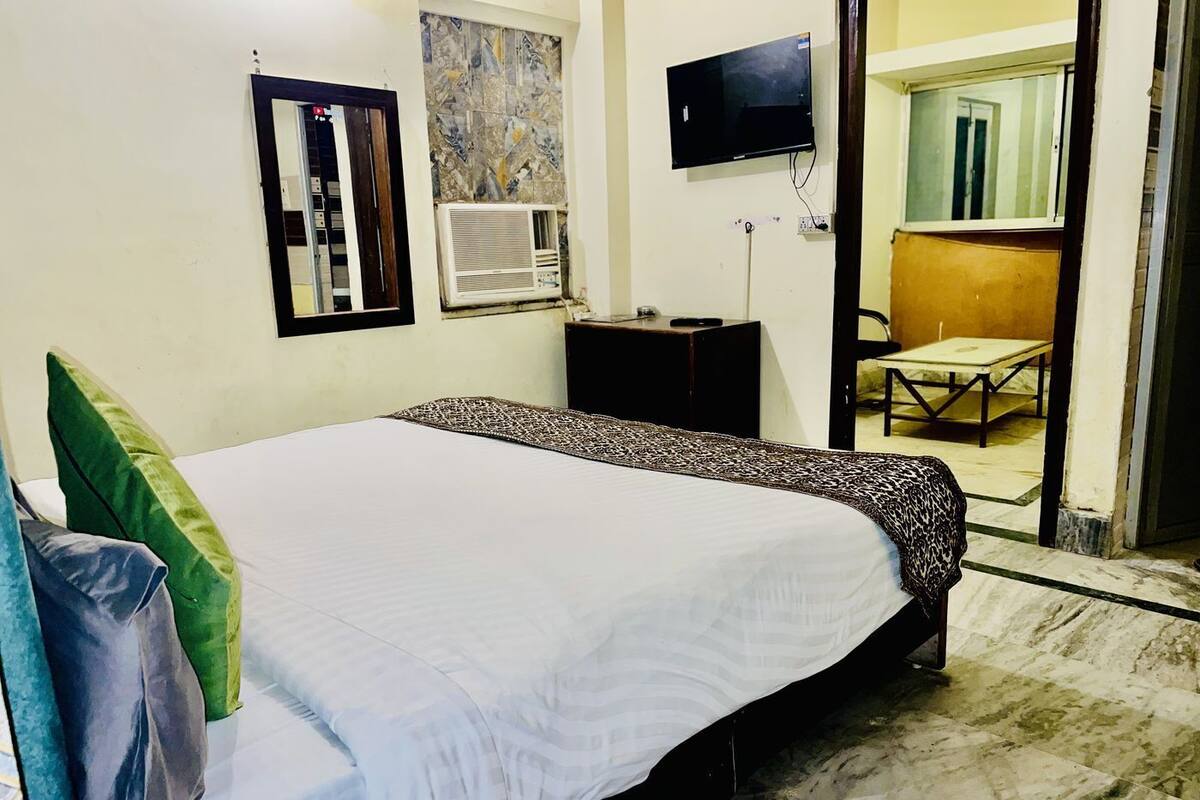 A hotel room with a bed, a TV, an air conditioning unit, a desk, and a chair.